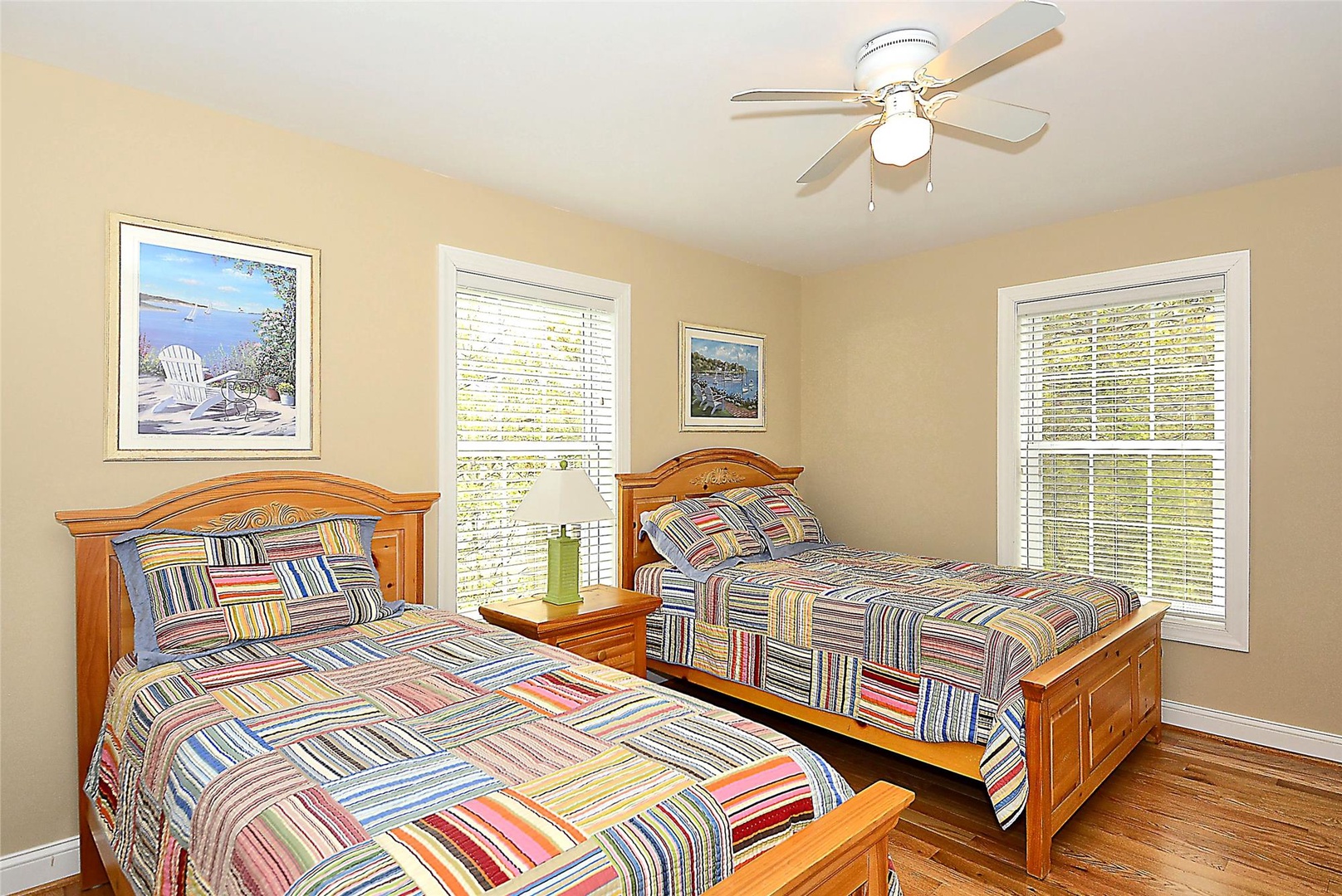 Unwind in your light-filled bedroom with twin beds dressed in cheerful linens, warmed by natural light streaming through multiple windows—perfect for restful mornings and peaceful nights.