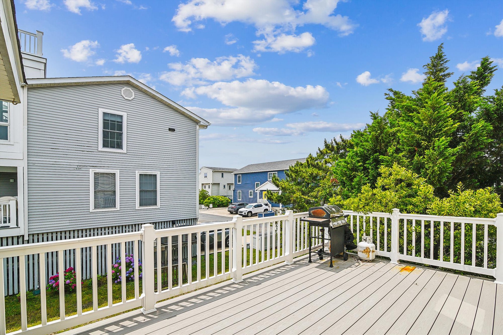 Spacious deck with BBQ, perfect for grilling while enjoying neighborhood views and fresh air under a bright blue sky.