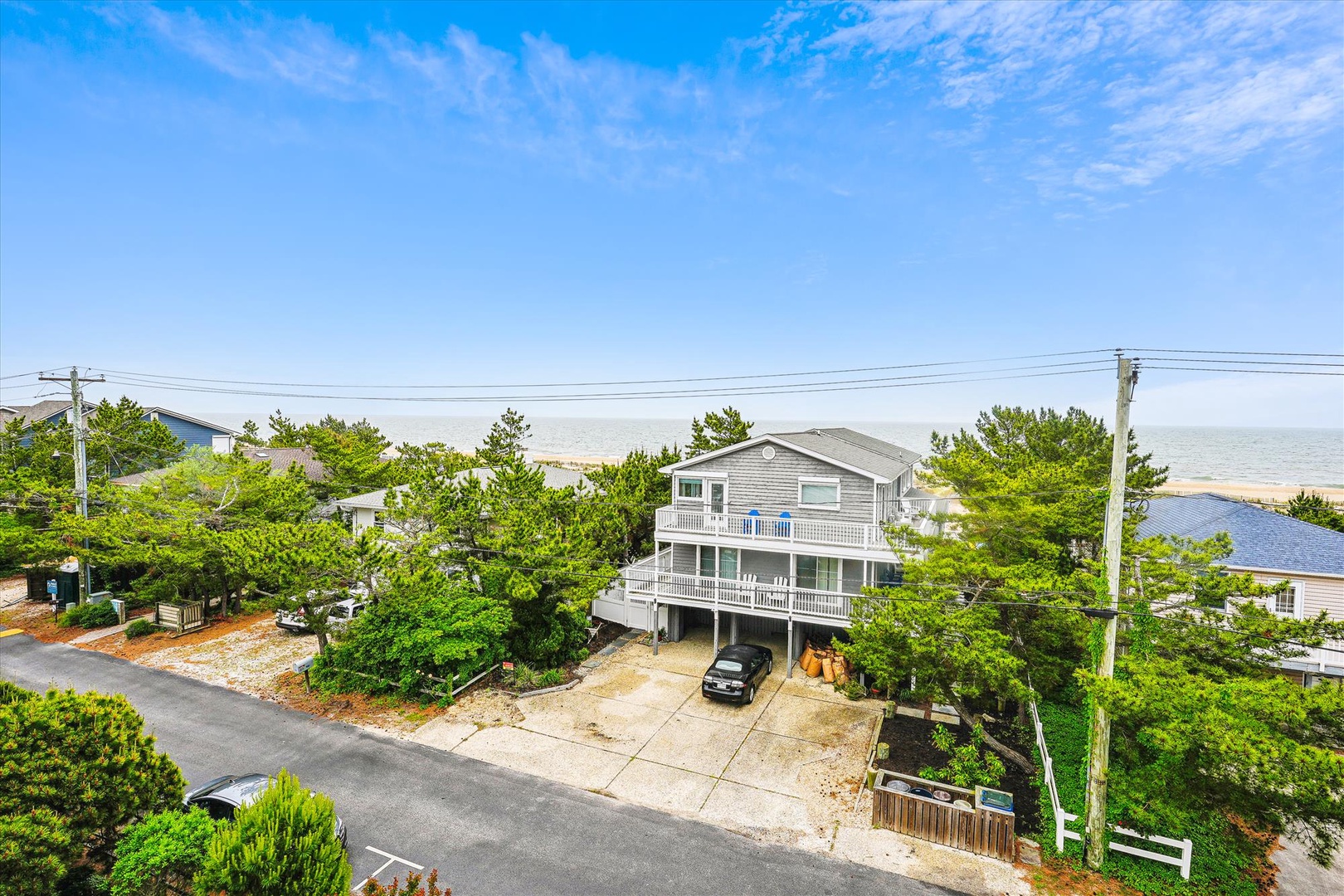 Aerial view of a spacious coastal property nestled among lush greenery, just steps from the beach and surrounded by a peaceful neighborhood.