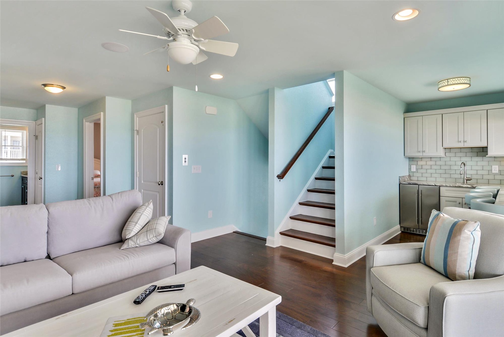 Unwind in your spacious living room, where soft blue tones, plush seating, and a ceiling fan create a breezy, relaxed vibe. The open kitchen layout makes it easy to chat, cook, and enjoy downtime together.