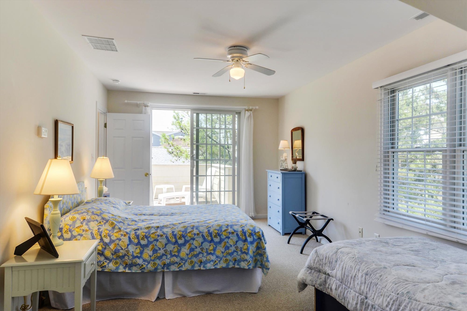 Your spacious bedroom welcomes you with coastal charm—two cozy beds dressed in beachy patterns, soft natural light streaming through the windows, and a private balcony just steps away for morning coffee.