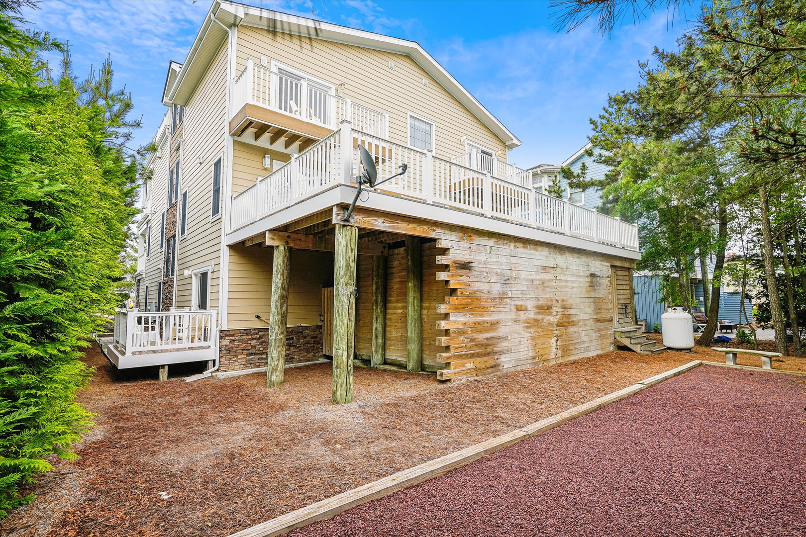 This charming coastal property features a spacious upper balcony, covered parking, and natural surroundings that offer a peaceful retreat surrounded by tall pines and greenery.