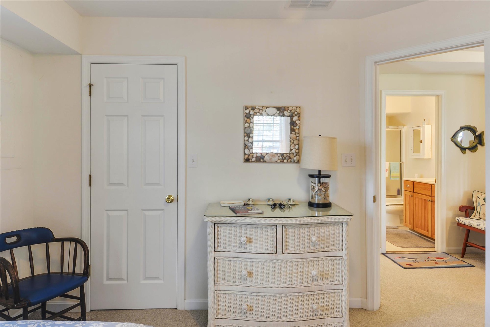 Step into your bright, airy bedroom featuring charming coastal decor and convenient access to your private bathroom. The wicker dresser and shell-framed mirror add a beachy touch to your relaxing retreat.