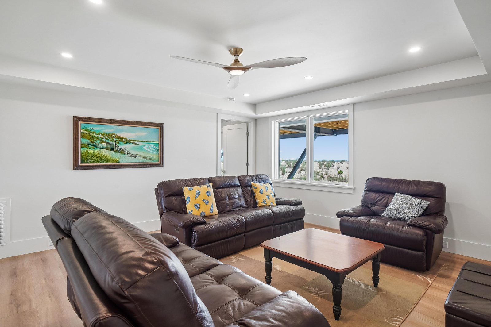 Sink into plush leather sofas and unwind in your bright, spacious living room, where sunny windows frame peaceful neighborhood views and a ceiling fan keeps you cool.