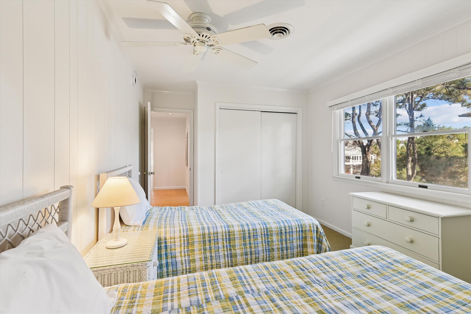 Your bright twin bedroom offers cheerful plaid bedding, peaceful treetop views, and gentle ceiling fan breezes for restful nights.