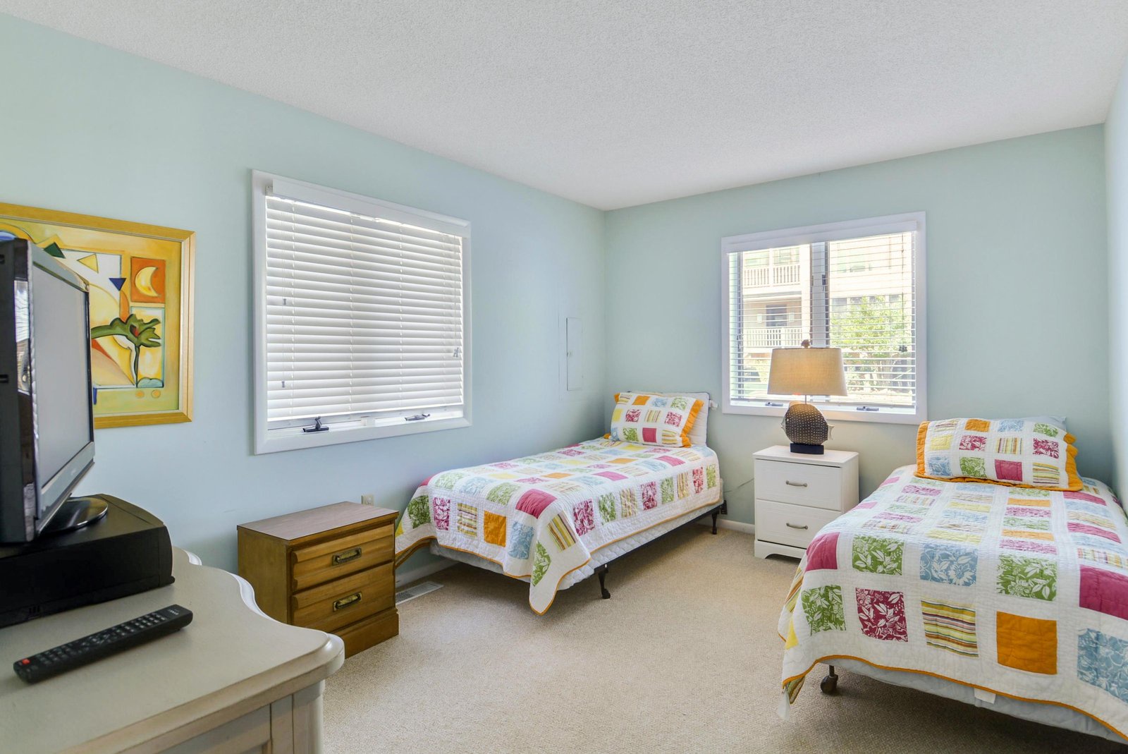 Cheerful twin beds with colorful quilts invite you to settle in. Soft morning light filters through the windows, and whimsical artwork adds a playful touch to your restful retreat.