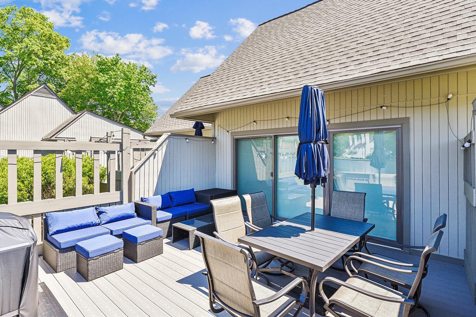Your private deck awaits with comfortable lounge chairs, outdoor dining, and a blue umbrella for shade—perfect for morning coffee or sunset cocktails while soaking in serene, tree-lined surroundings.