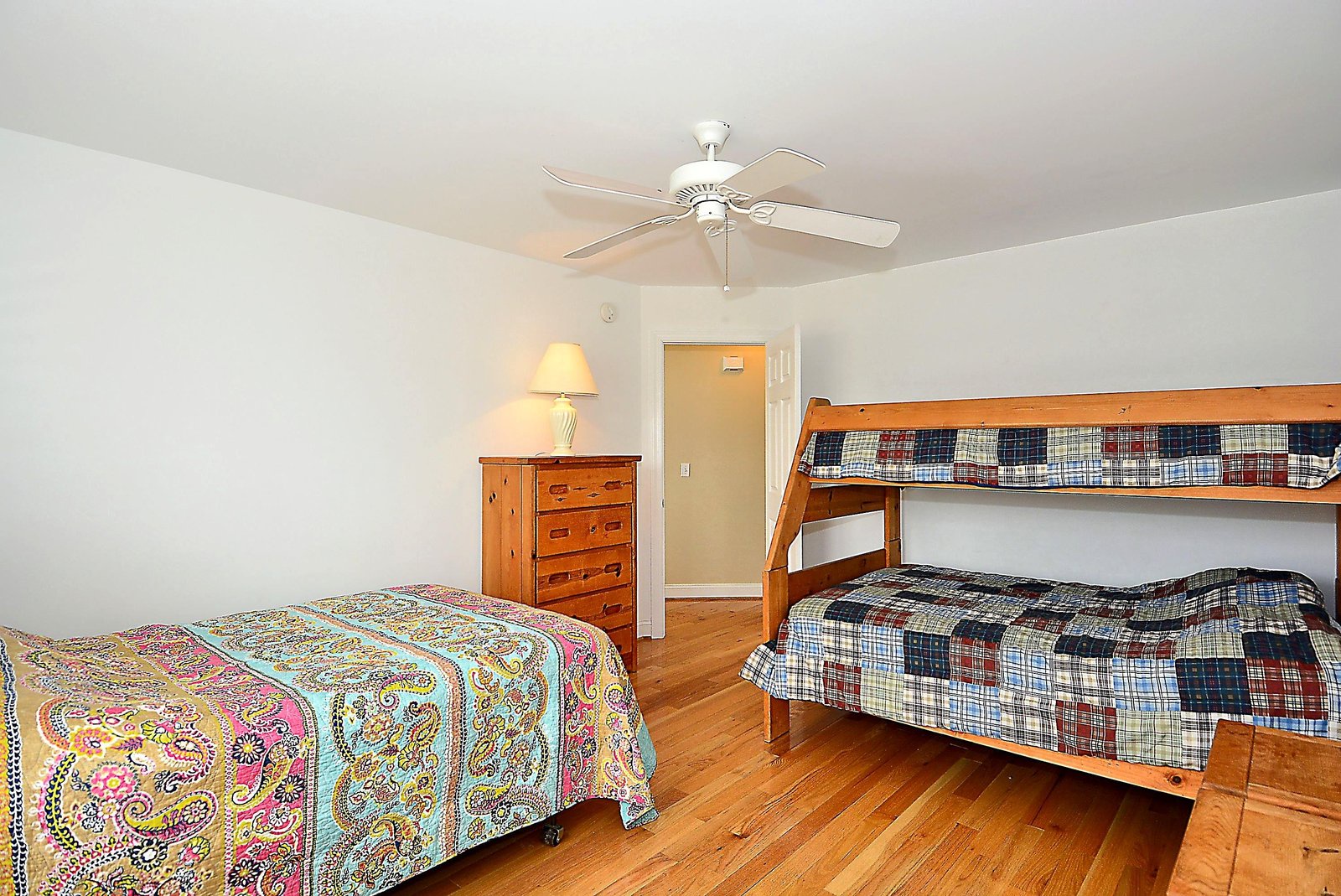 Rest easy in your comfortable bedroom featuring a queen bed and fun bunk beds perfect for kids or extra guests, all kept cool by a ceiling fan overhead.