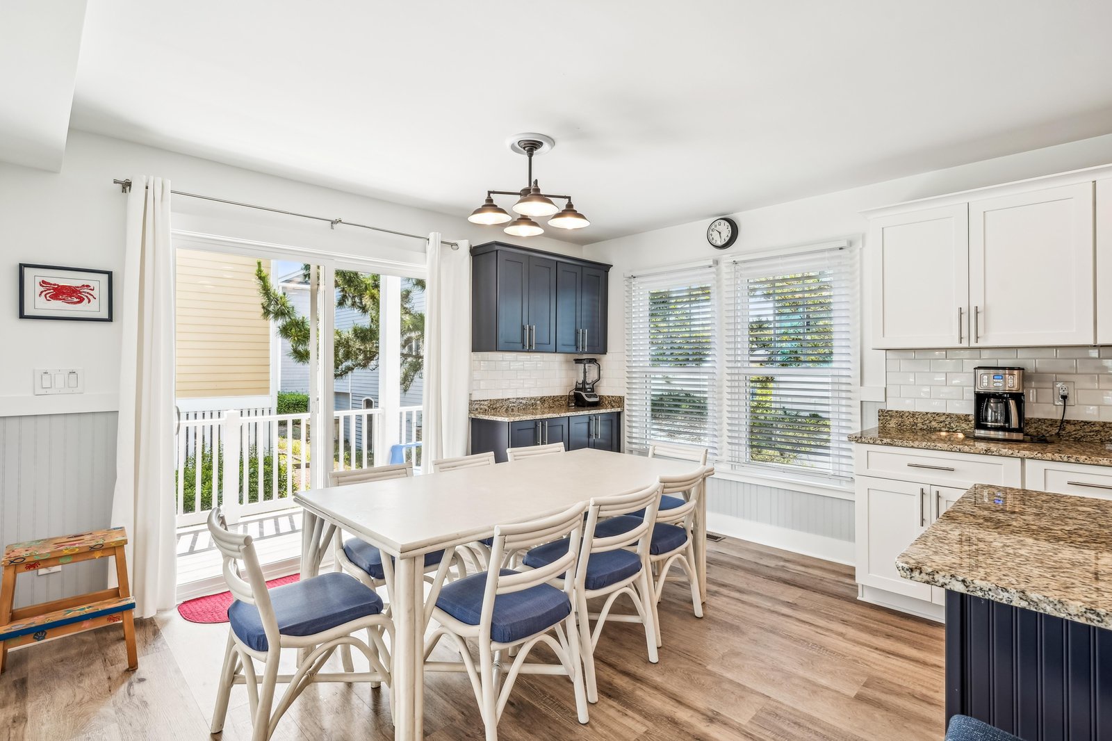 A bright kitchen and dining space where you'll gather for morning coffee and meals together. White cabinetry pairs with charming nautical touches, and sunlight streams through glass doors opening to your private deck.