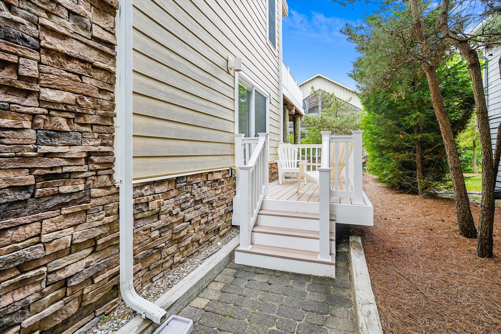 The property features a welcoming entrance with a charming white deck and stairs, surrounded by mature trees and peaceful natural surroundings in a quiet residential area.