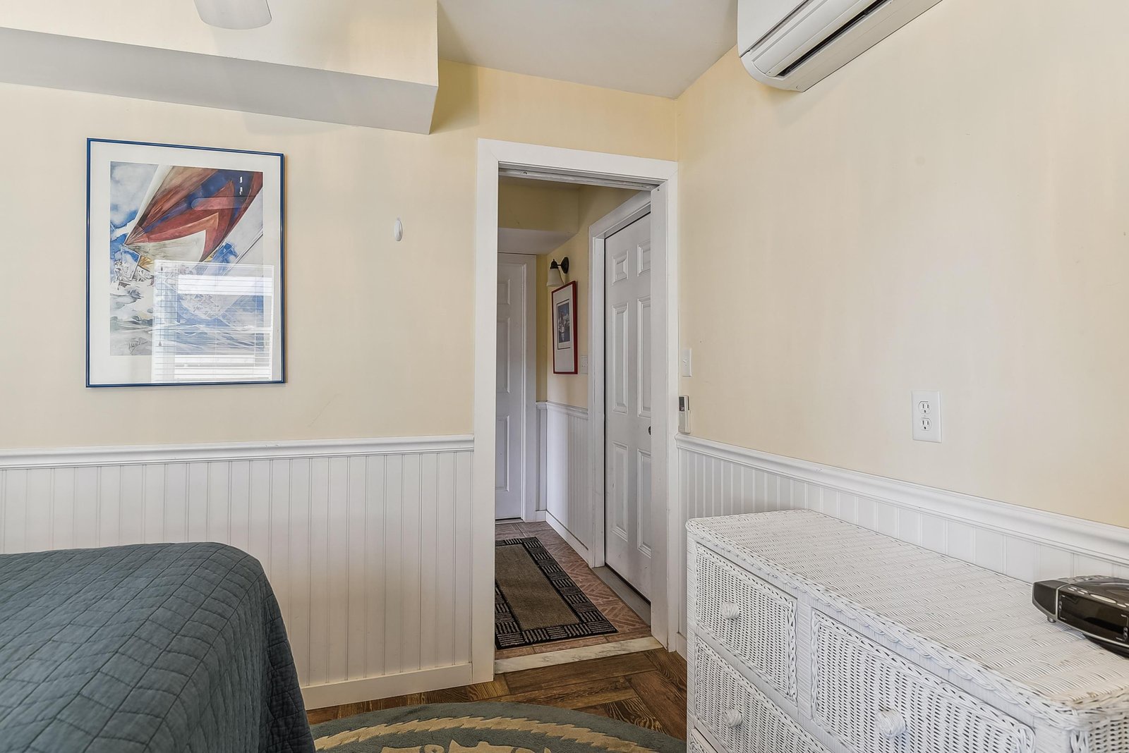 Your coastal bedroom offers a calming palette of cream and soft blue with charming wainscot trim, air conditioning for comfort, and a view into the hallway.
