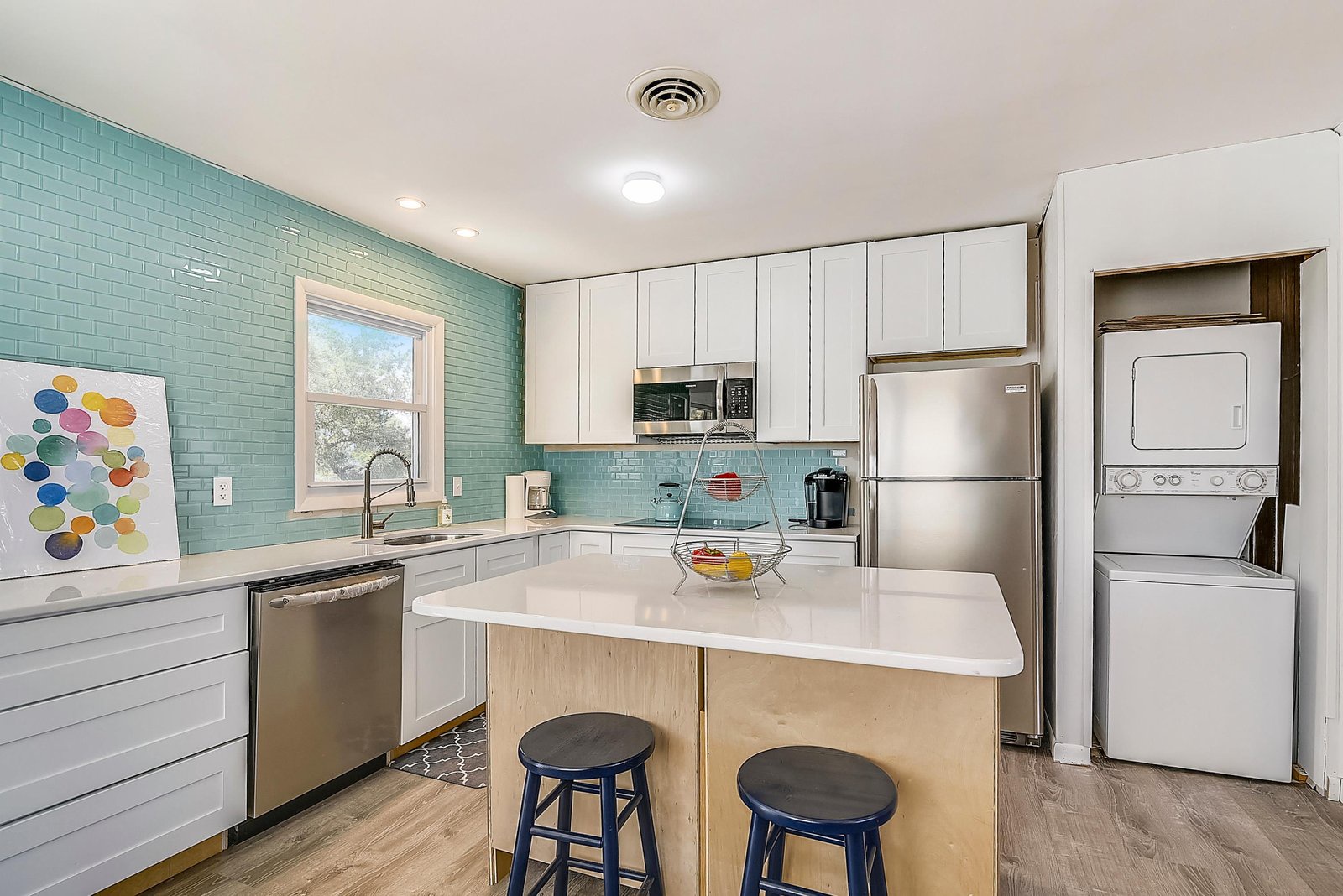 Step into your cheerful kitchen where glossy turquoise tile meets bright white cabinetry. Prep your morning coffee at the island or whip up a meal with stainless appliances—everything you need is right here.