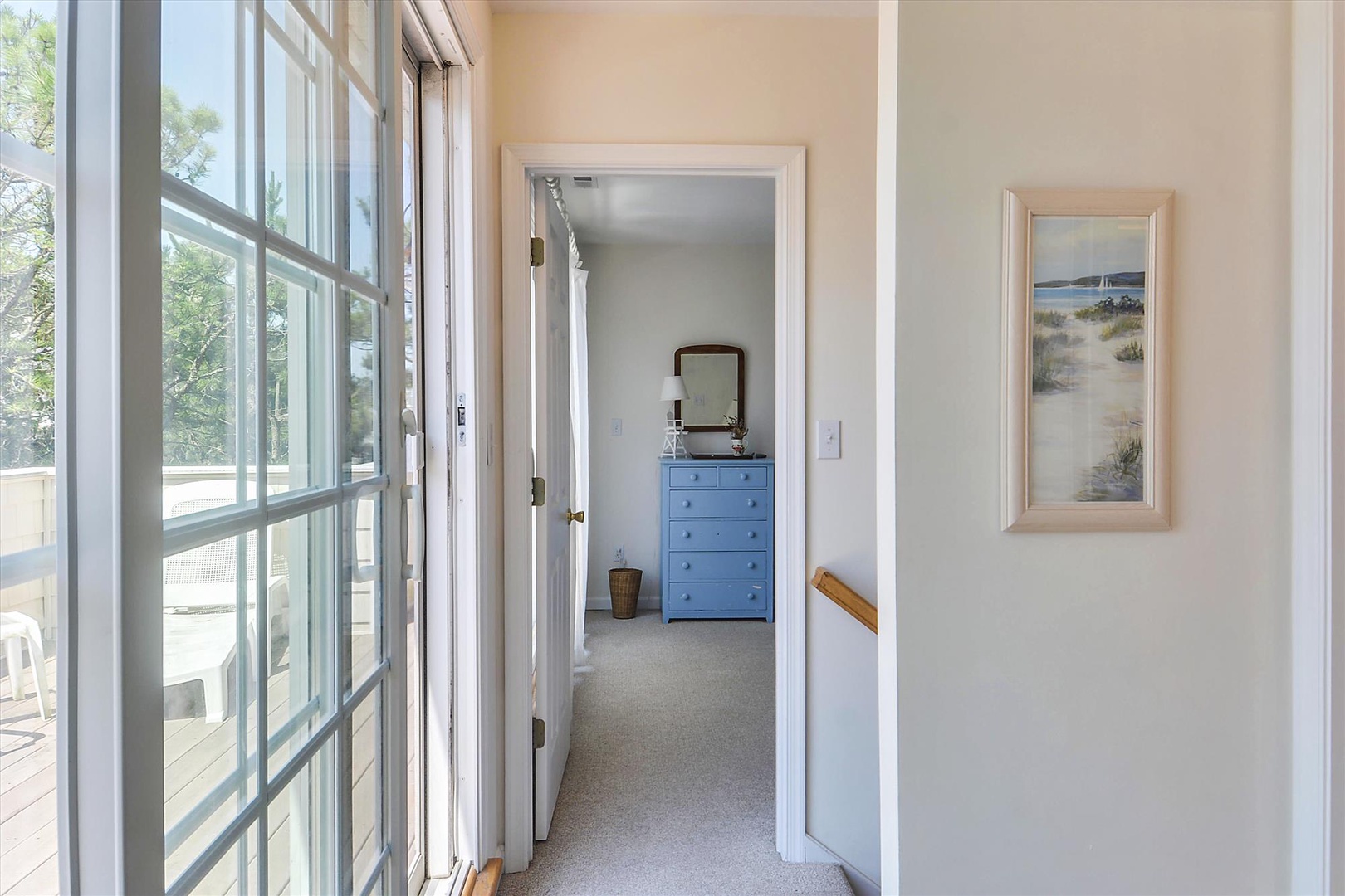 Step through these bright doors into your peaceful bedroom retreat, where coastal charm and comfort await you. Soft sunlight illuminates the serene blue dresser and beachside artwork.
