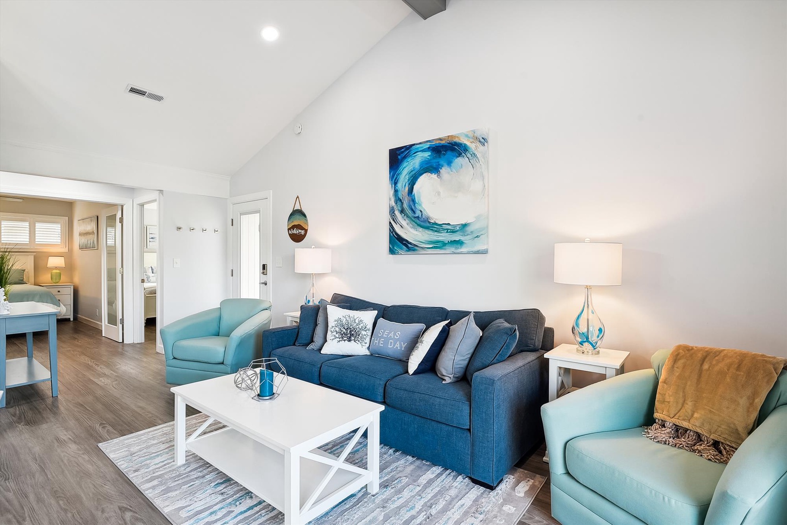 Relax in your bright living space with plush blue seating, ocean-inspired art, and vaulted ceilings that create an airy coastal vibe.