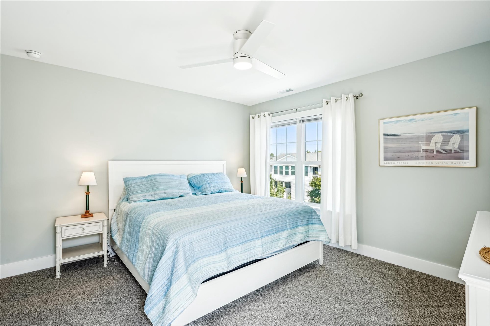 Drift off to sleep in your serene coastal bedroom, where soft blue linens and gentle ceiling fan create the perfect retreat.