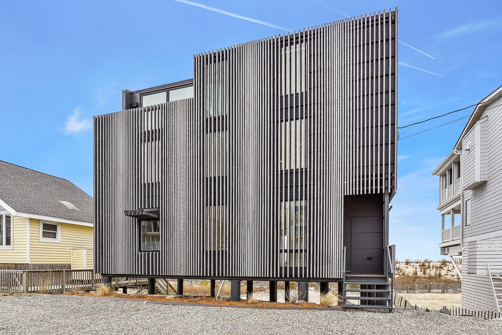 Modern coastal architecture with distinctive vertical slat design set in a beachside neighborhood, offering an elevated style among neighboring homes.
