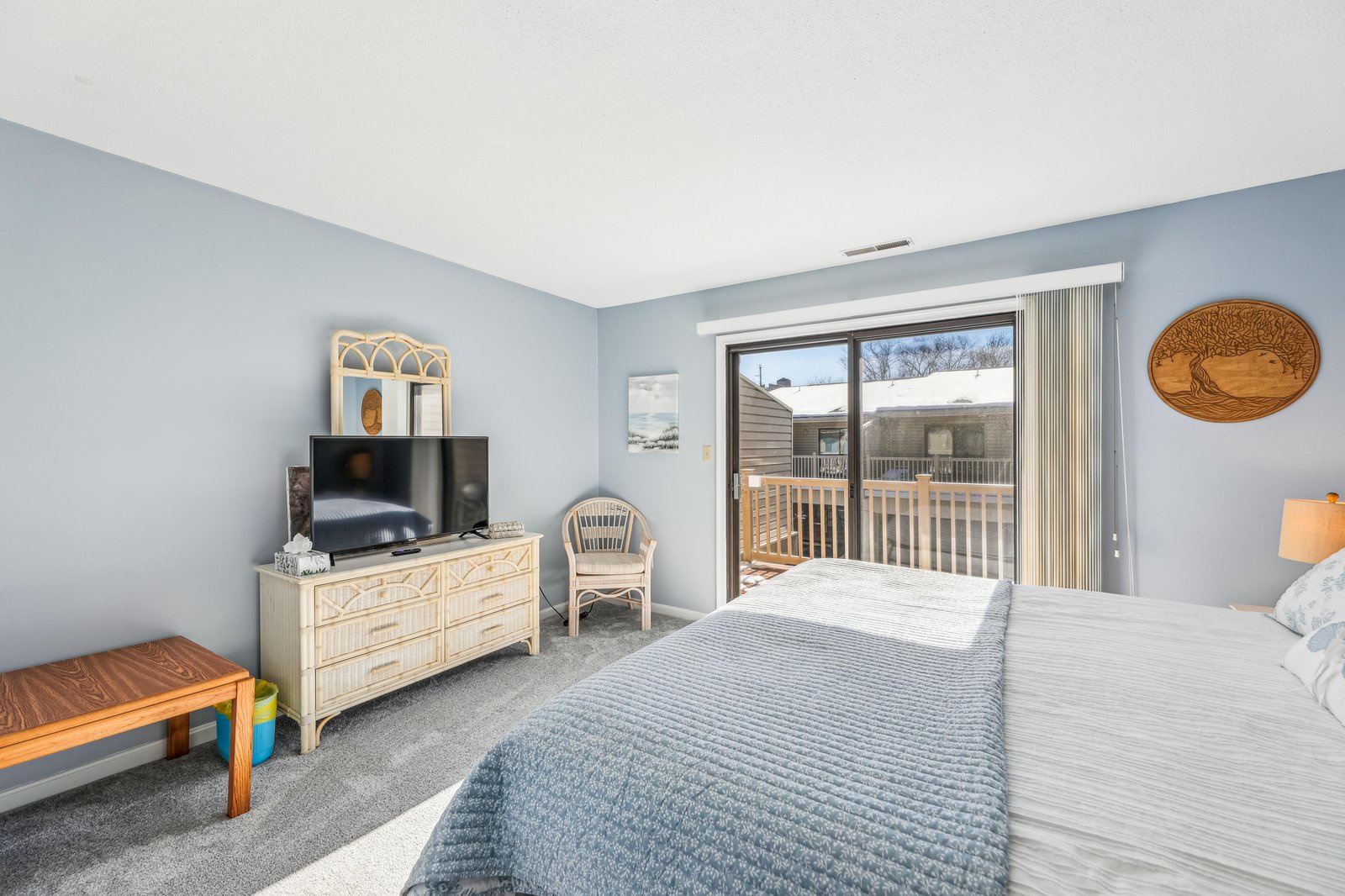 Wake up to natural light and step directly onto your private deck through sliding glass doors. Soft coastal-blue walls and a cozy bed invite restful mornings, while your outdoor space awaits just beyond the glass.