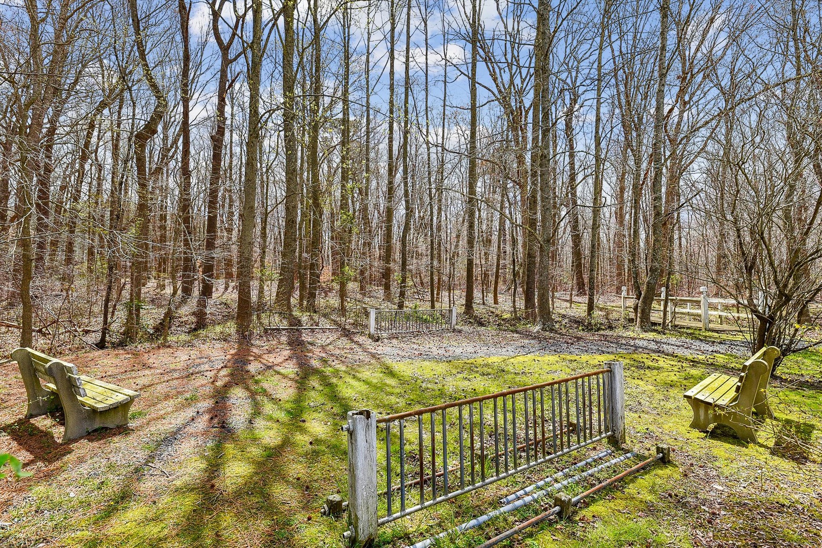 Peaceful wooded setting surrounds the property with benches and natural walking paths through bare winter trees and emerging spring moss.