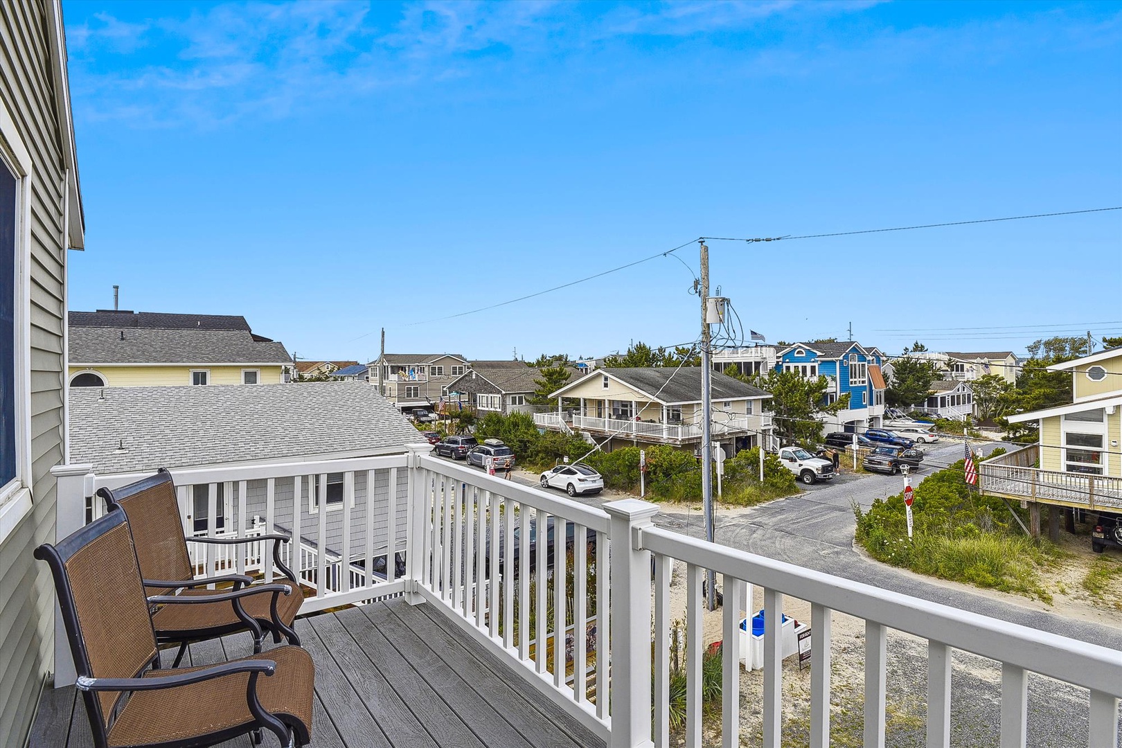 A coastal neighborhood with nearby beach access surrounds the property, featuring a mix of vacation homes and local residences under clear blue skies.