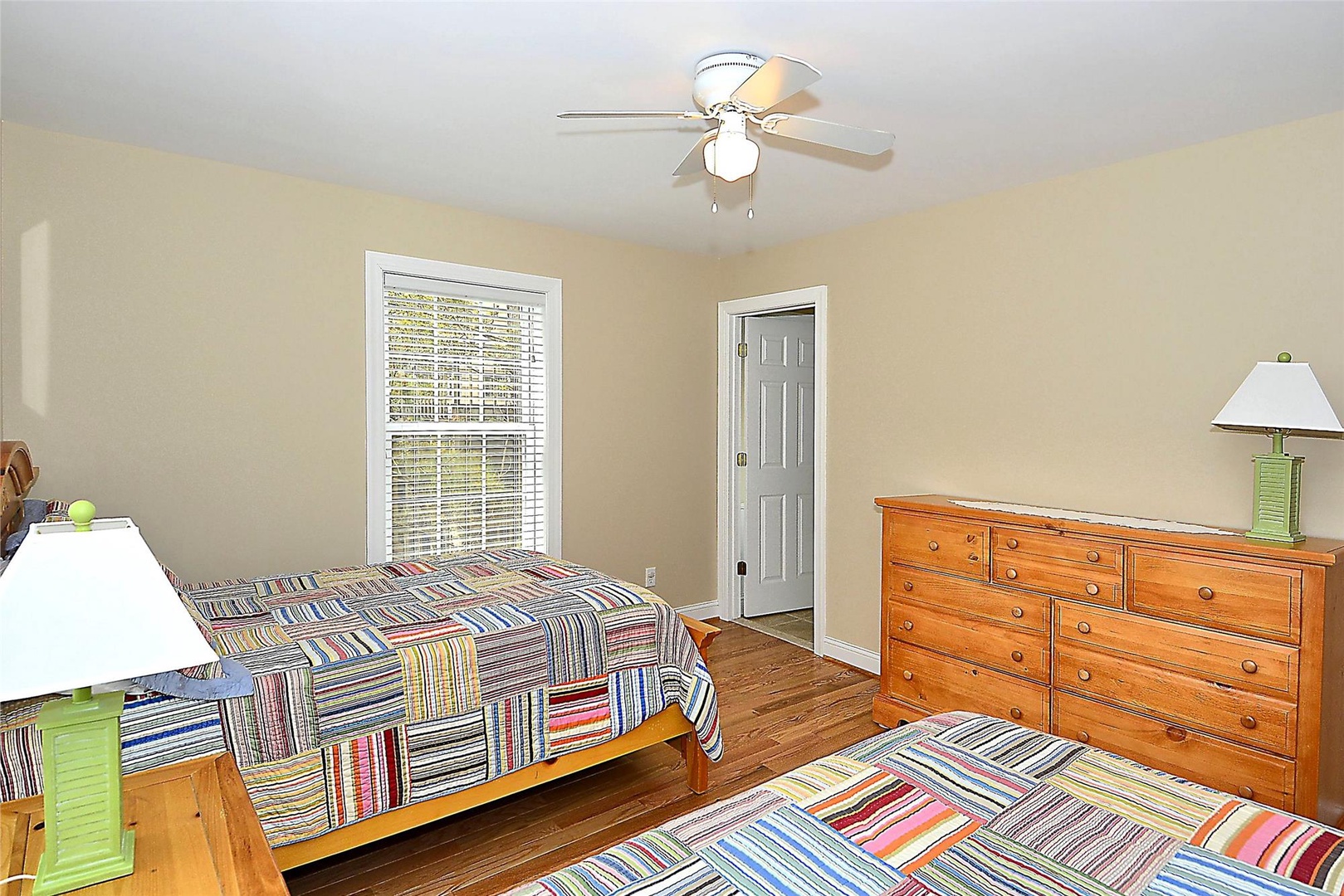 Your bright, spacious bedroom features warm hardwood floors, cheerful striped bedding, ample dresser storage, and a ceiling fan to keep you comfortable year-round.