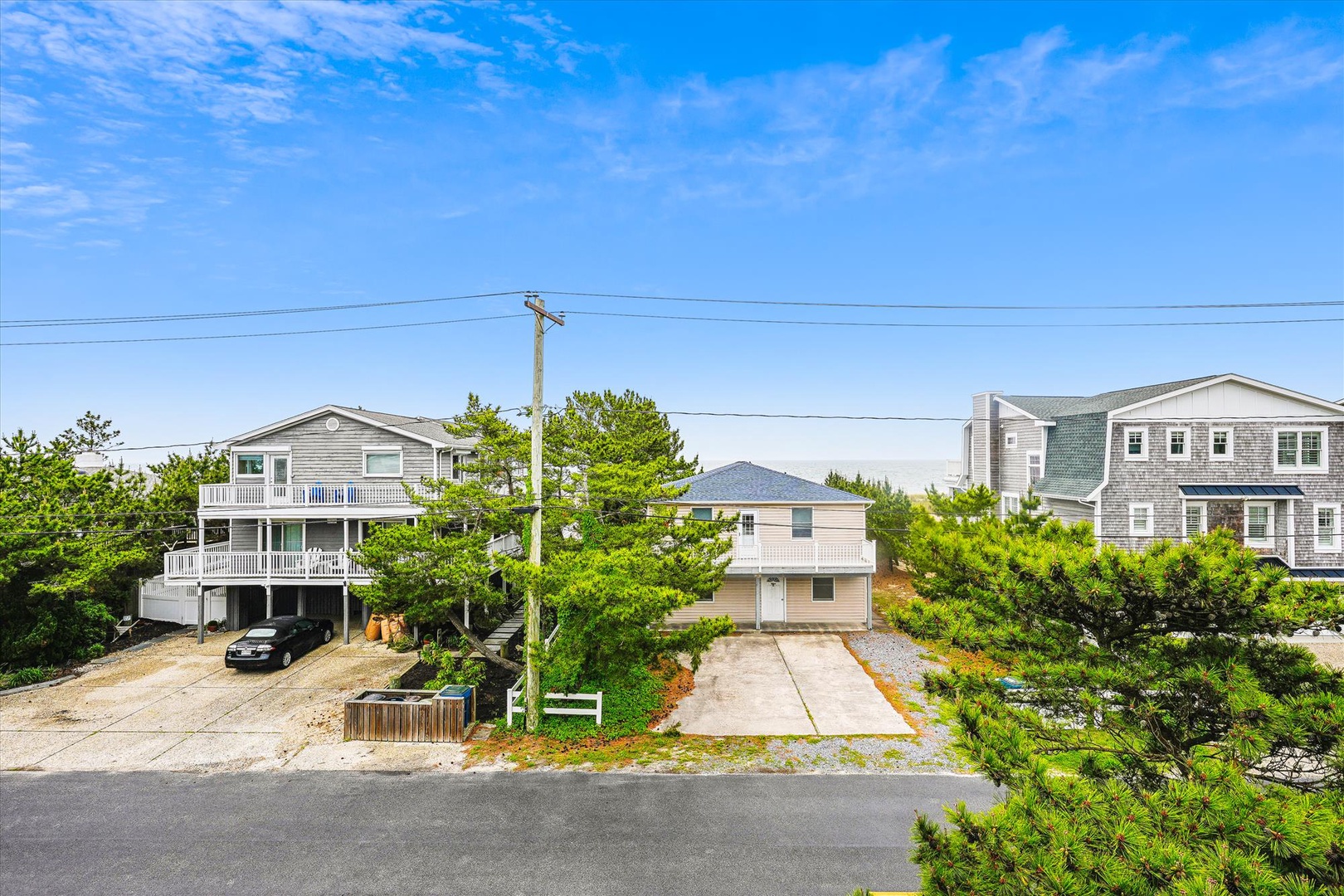 A coastal neighborhood with beach houses nestled among mature pines, just moments from the shore with convenient parking and easy access.