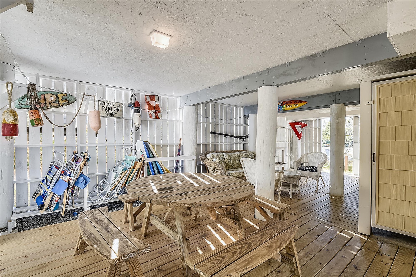 This covered porch offers a relaxed coastal vibe with picnic-style seating, vintage beach decor, and wicker chairs—perfect for dining or unwinding after a day by the water.
