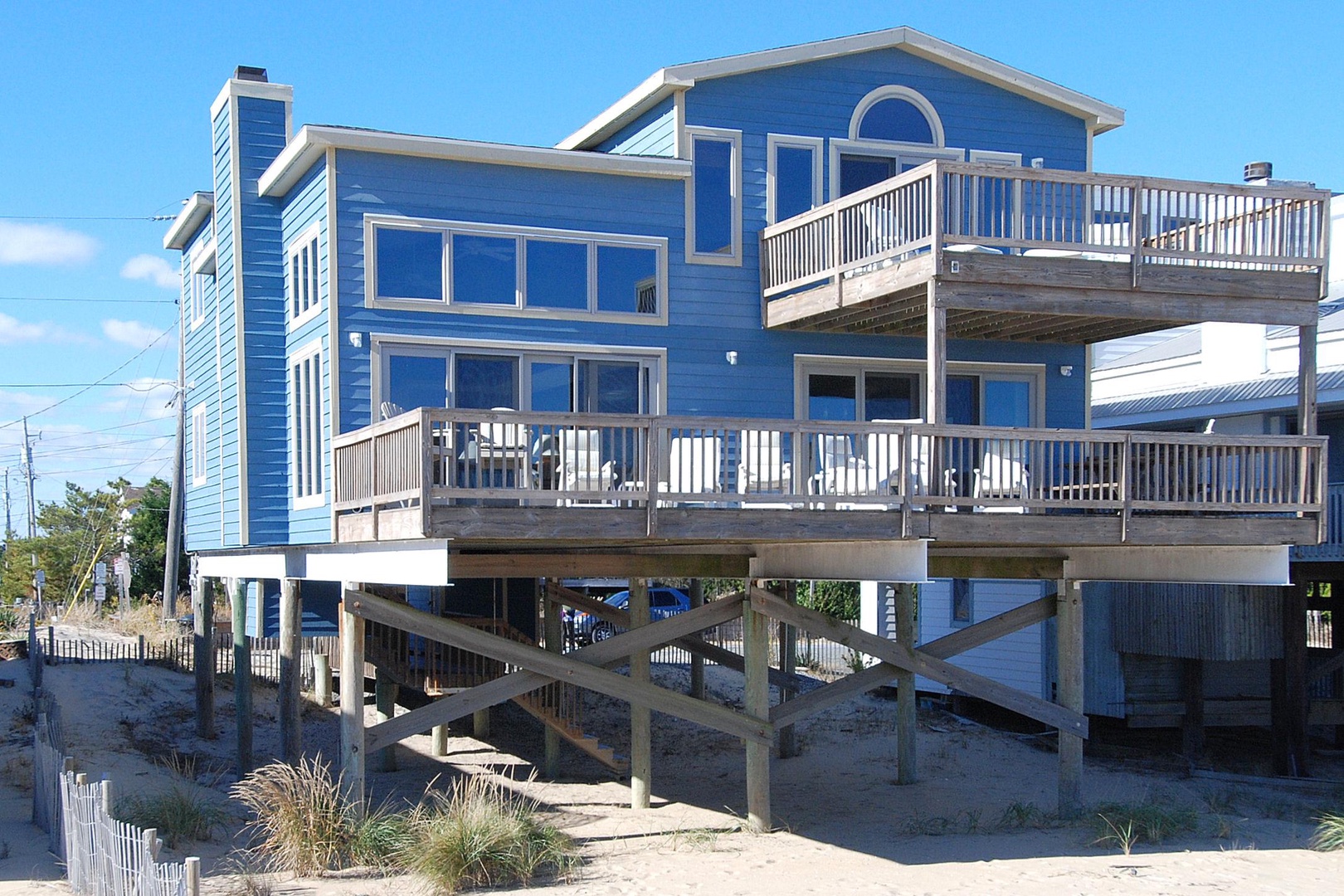 Elevated blue beachfront property with wraparound decks and coastal design, situated directly on sandy shores.
