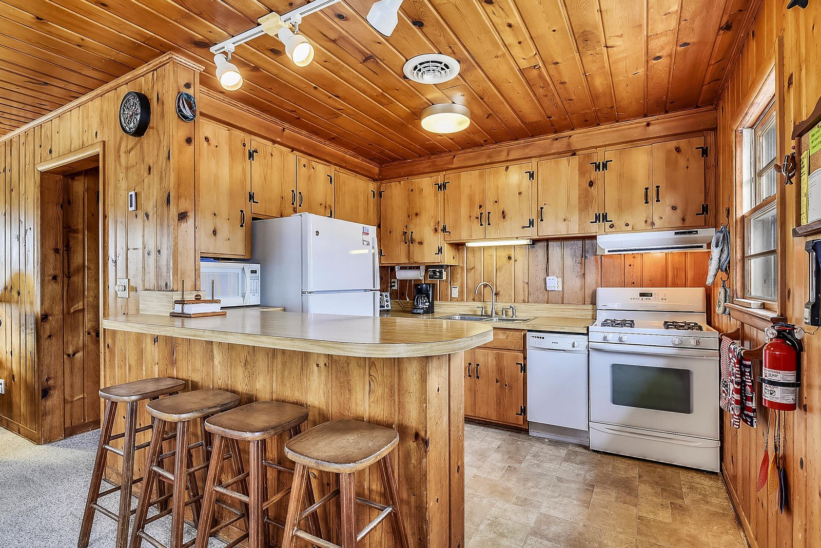 Your fully equipped kitchen blends rustic charm with modern convenience, featuring warm knotty pine throughout, stainless steel appliances, and a breakfast bar perfect for morning coffee or casual meals.