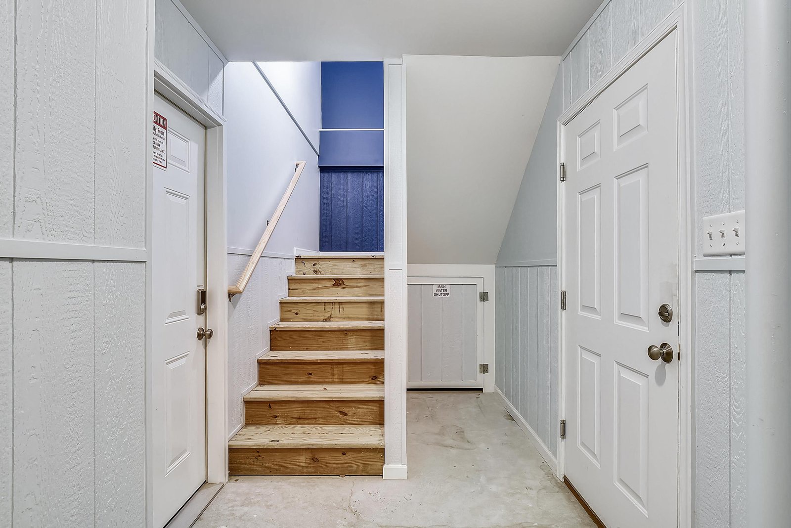 The lower-level entry welcomes you with clean lines and coastal-inspired blue hues visible on the stairs ahead, guiding you up into your home away from home.