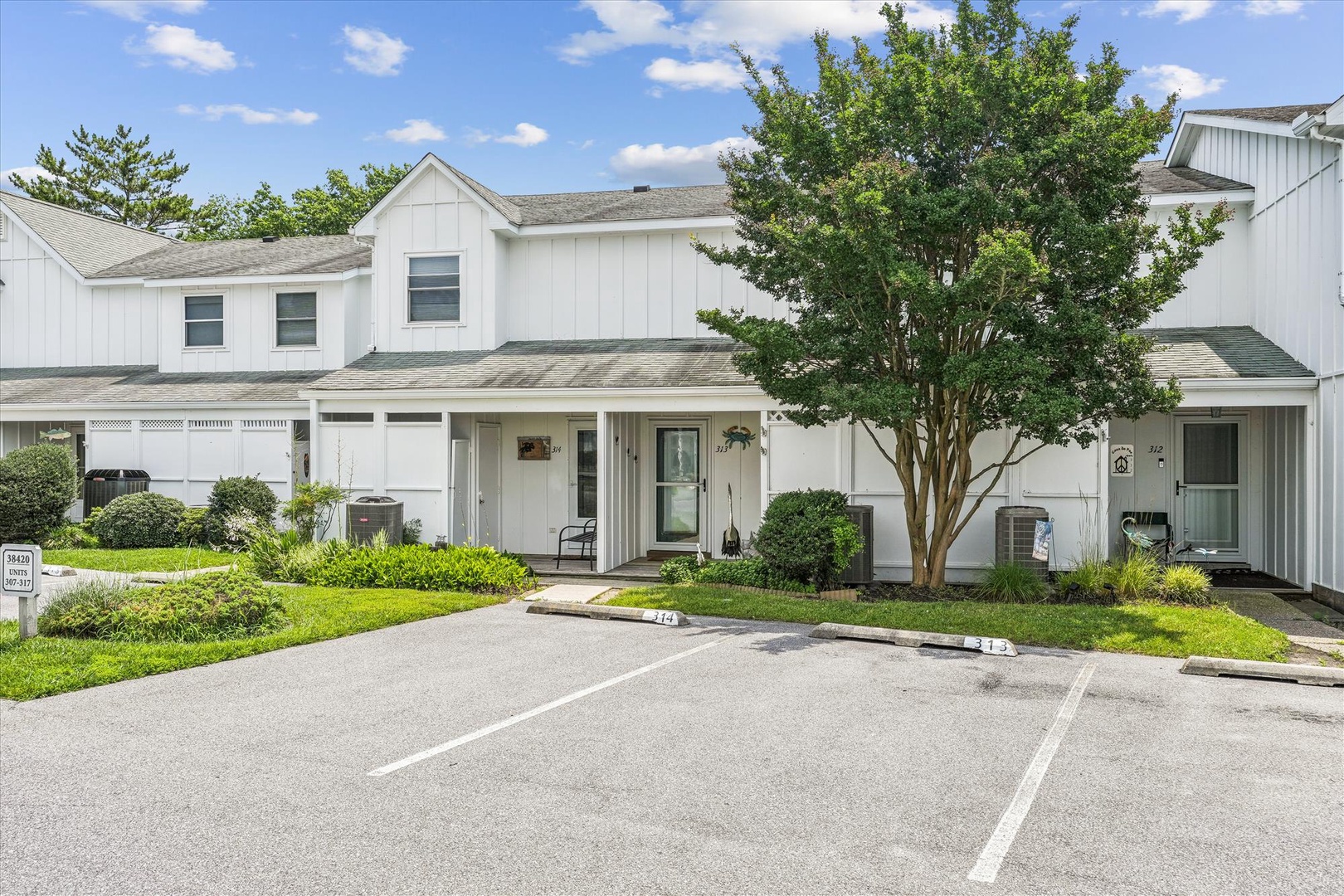 White two-story townhouse with covered front porch, landscaped yard, and designated parking in a quiet residential community setting.