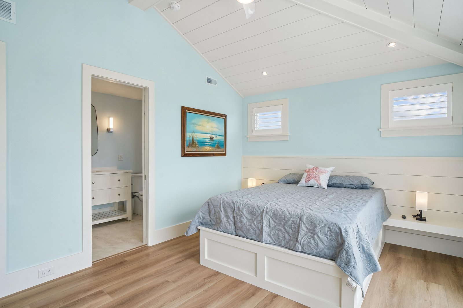 Drift off in your serene coastal bedroom, where soft blue walls and shiplap accents create a calming seaside escape. Natural light streams through charming windows as you unwind in peaceful comfort.