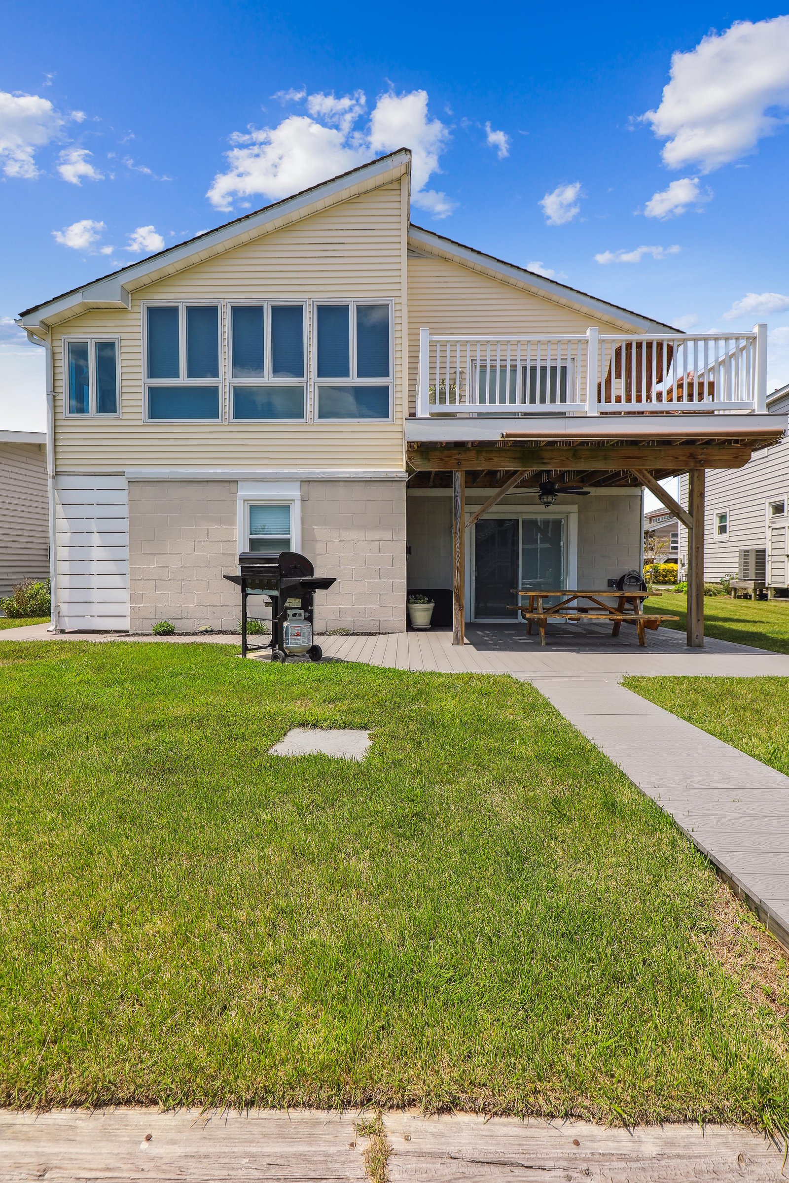 A charming two-story coastal home with an upper deck and covered patio, featuring BBQ facilities and lawn space—perfect for relaxed outdoor gatherings.