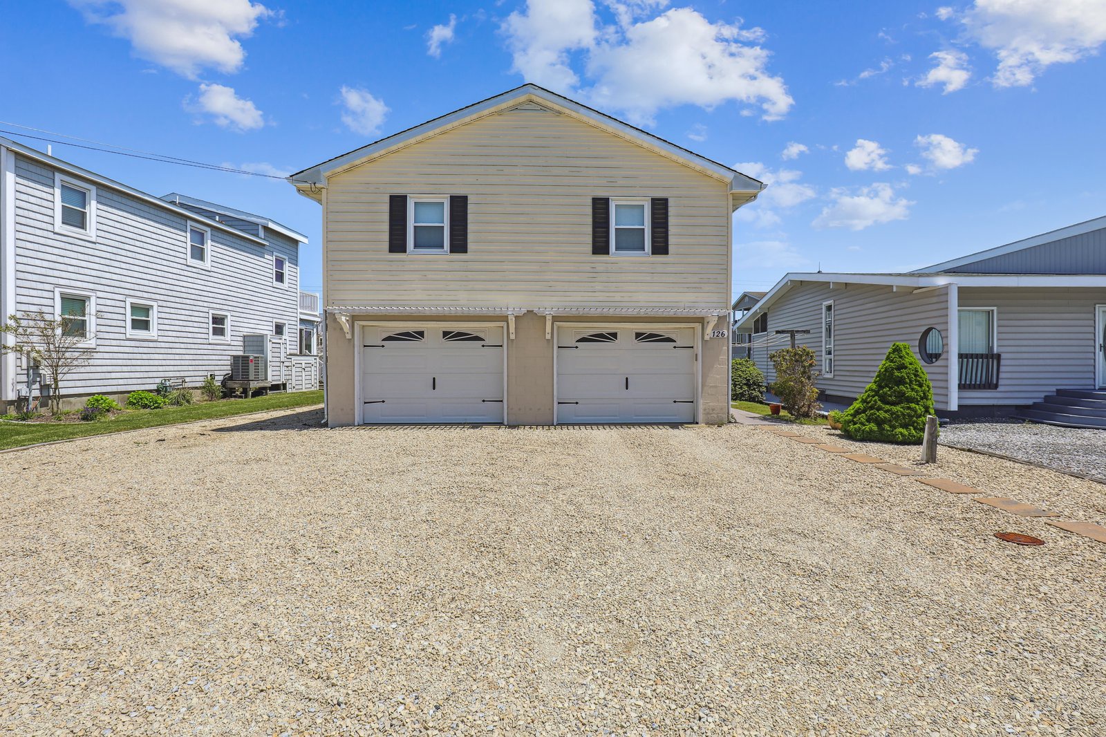 Coastal home featuring a spacious two-car garage and generous gravel driveway parking in a quiet residential neighborhood.