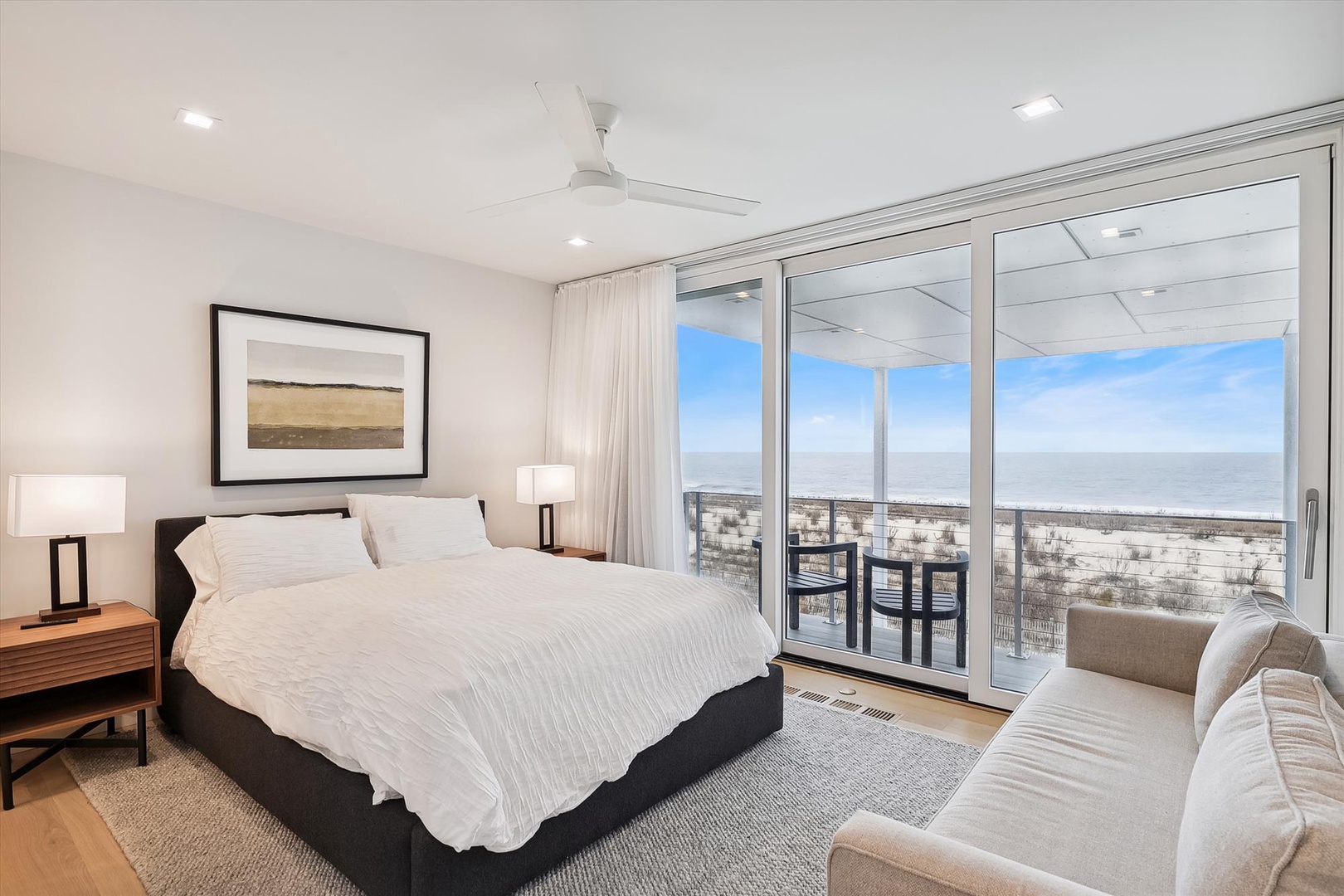Wake up to breathtaking ocean views through floor-to-ceiling windows. Your serene bedroom features a plush bed, modern furnishings, and direct balcony access to soak in coastal breezes.