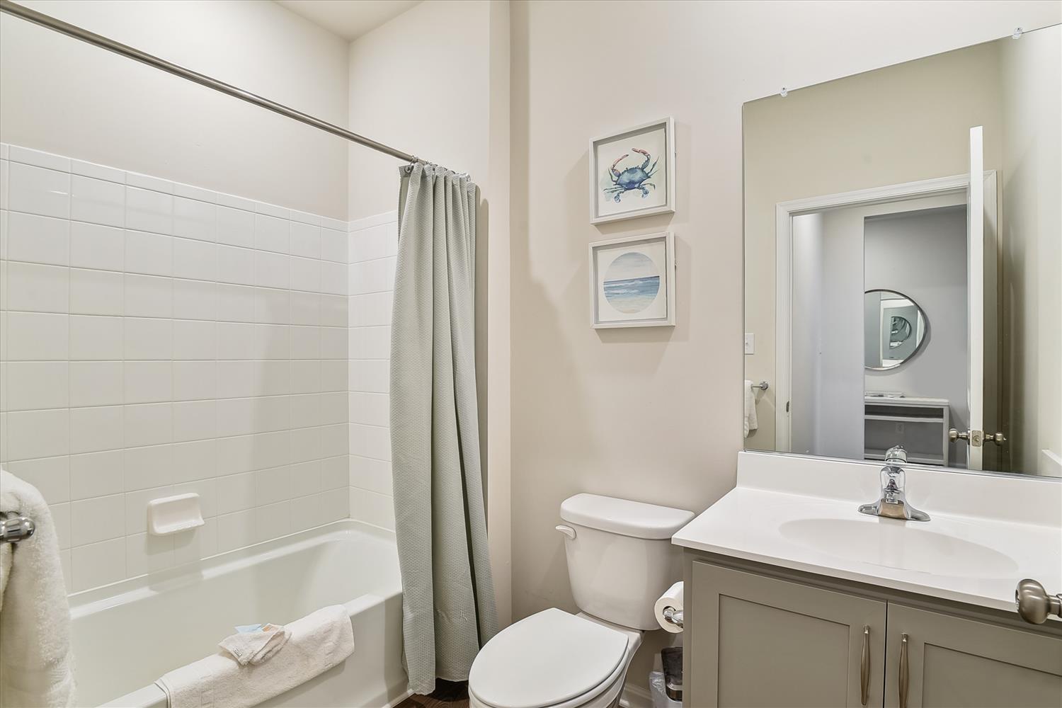 Step into your pristine private bathroom, where coastal charm meets modern comfort with soothing beach-themed art and fresh towels awaiting your arrival.