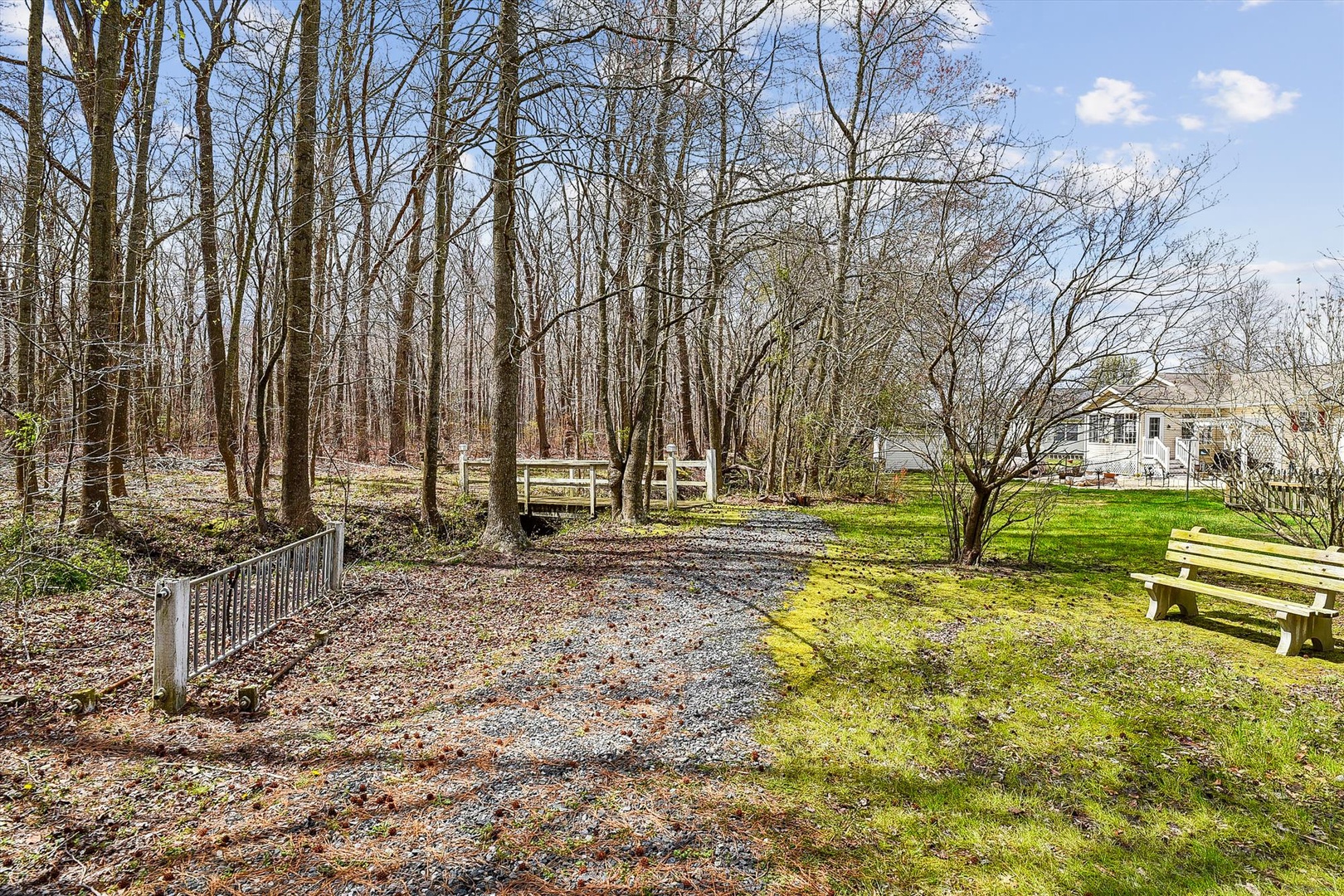 The property sits on a tranquil wooded lot with mature trees, a gravel pathway, and peaceful natural surroundings—ideal for those seeking a quiet, nature-filled retreat.