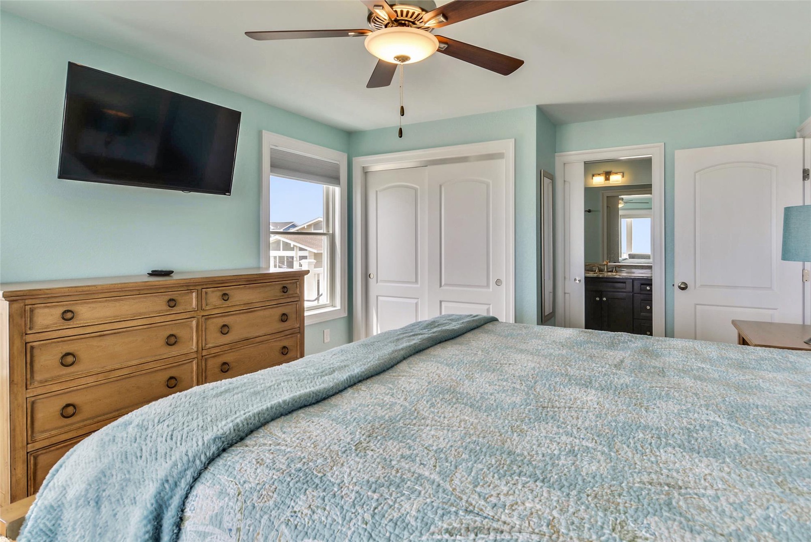 Sink into the soft aqua bedding of your serene bedroom retreat, where soothing coastal hues and a gentle ceiling fan invite you to unwind and recharge.