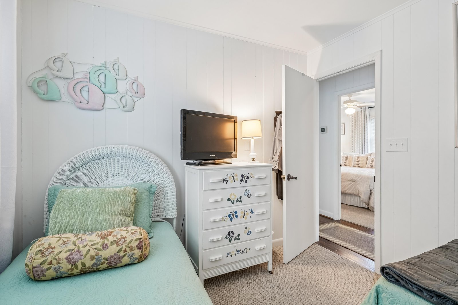 Step into your bright coastal bedroom featuring charming beachy decor, turquoise accents, a flat-screen TV, and easy access to the adjacent master suite. A perfect spot to unwind after sunny beach days.
