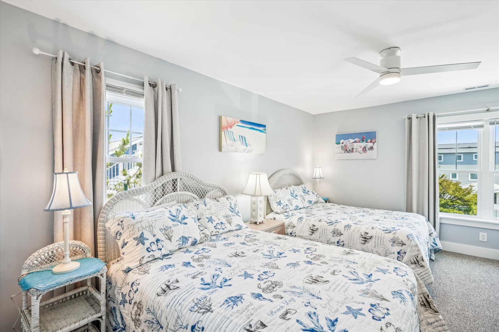 Drift off in this serene bedroom featuring two comfortable beds adorned with coastal-themed linens and gentle ocean breezes from your ceiling fan.