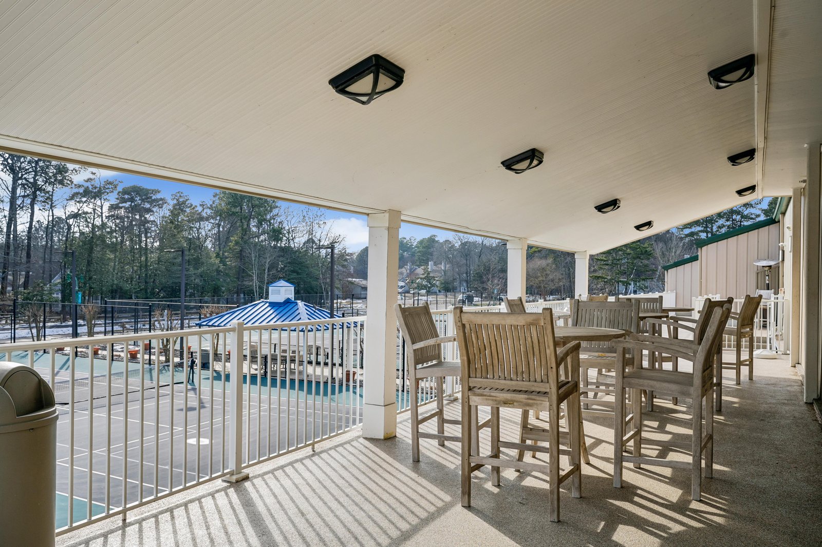 Covered patio seating overlooks the sparkling pool area, surrounded by tall pines and natural woodlands—perfect for relaxing between swims.