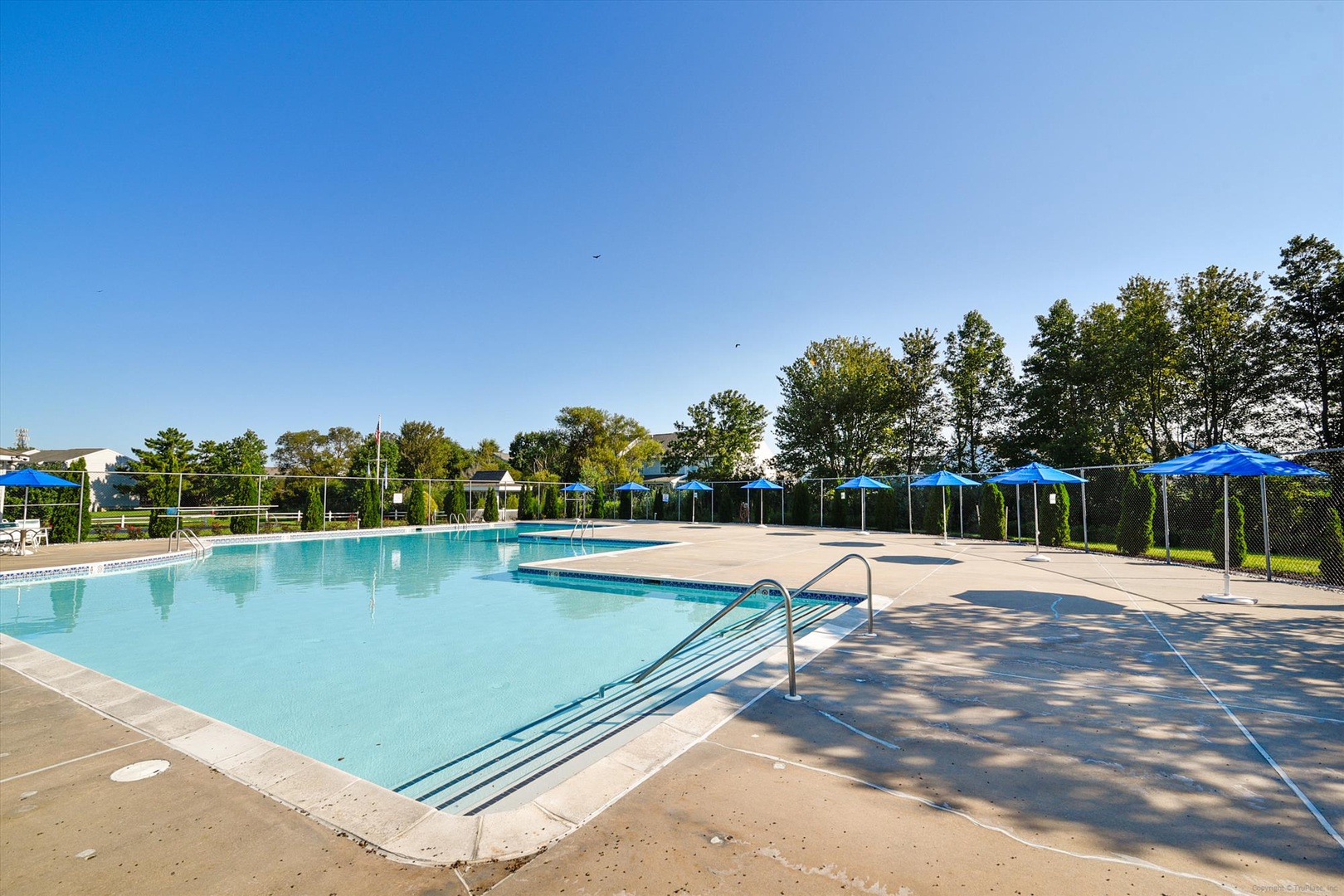 Spacious outdoor swimming pool with accessible entry, surrounded by shaded lounging areas and verdant trees for sun-soaked relaxation.