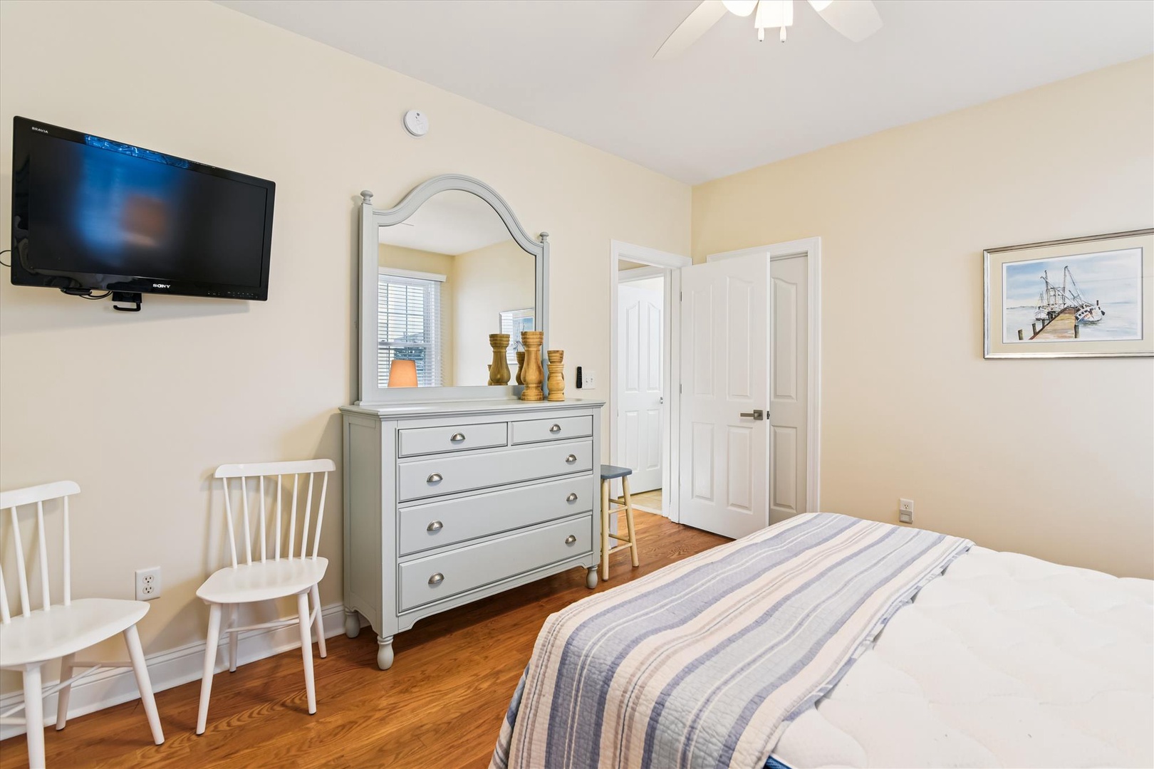 Unwind in your cozy bedroom with a wall-mounted TV, nautical touches, and plenty of storage. The classic dresser and hardwood floors create a relaxed coastal retreat.
