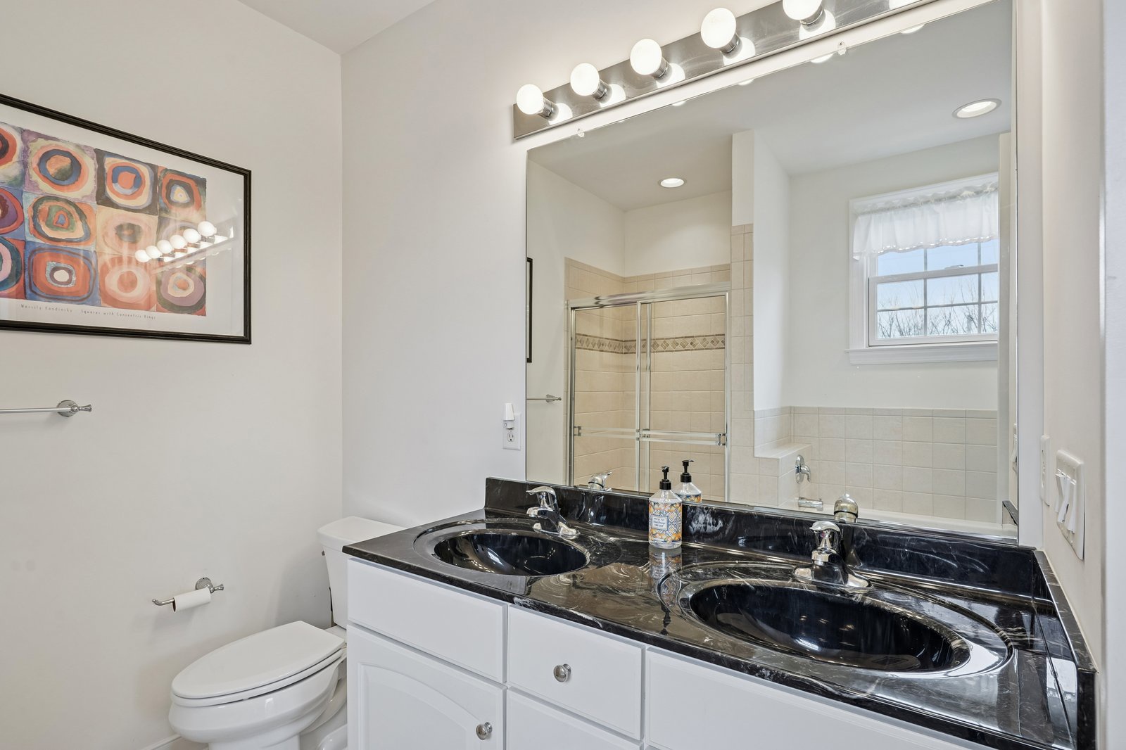 Freshen up in your elegant bathroom featuring dual sinks with sleek black granite countertops and bright vanity lighting.
