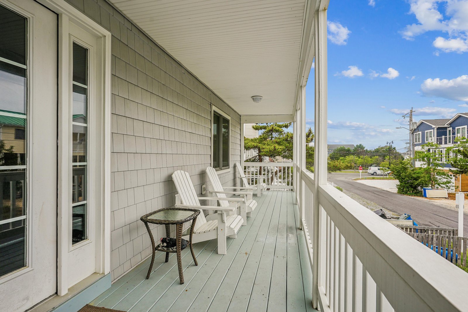 Your private porch welcomes you with Adirondack chairs and a cozy table, perfect for morning coffee or watching the coastal neighborhood unwind beneath blue skies.
