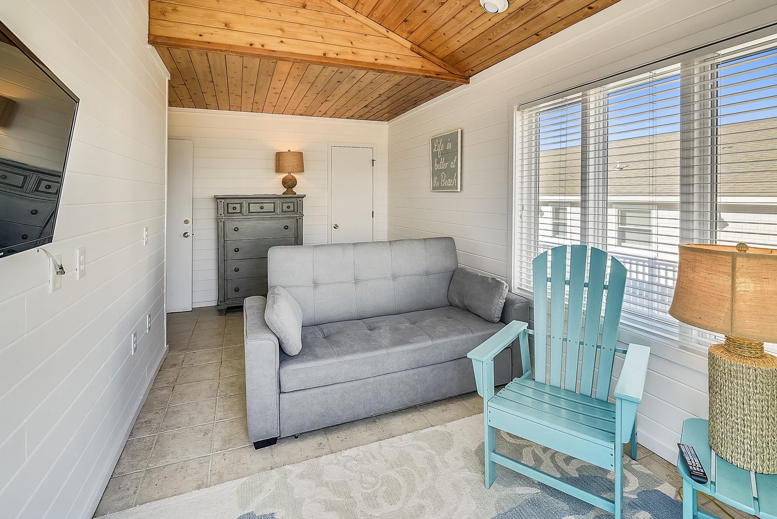 Your cozy cottage living room awaits with warm wood ceilings, a comfy pull-out sofa, and coastal charm. Sink into the bright turquoise chair, soak in natural light from oversized windows, and feel instantly at home in this inviting retreat.