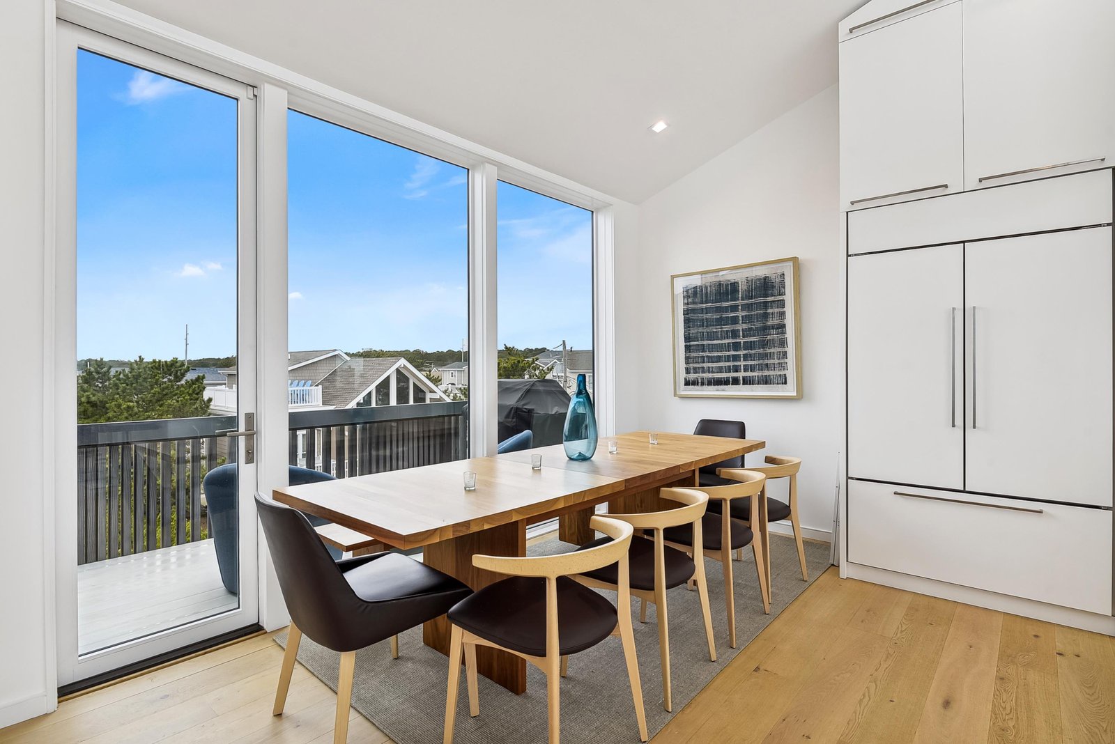 Your bright dining space opens directly onto your private deck, where rooftops and greenery stretch into the distance. Natural light pours through three glass doors, making every meal feel effortless.