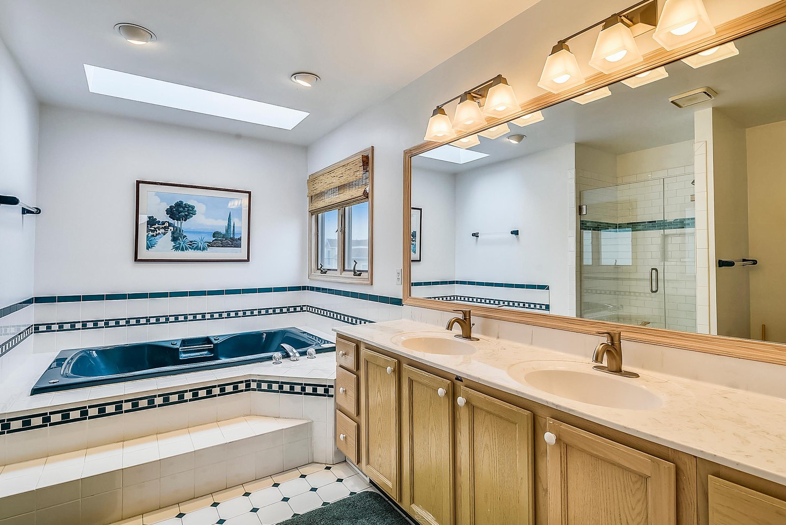 Luxurious bathroom with a deep soaking tub, elegant tiled accents, dual sinks, and a spacious glass-enclosed shower. Natural light pours in through a skylight, creating a bright and refreshing retreat for your daily rituals.