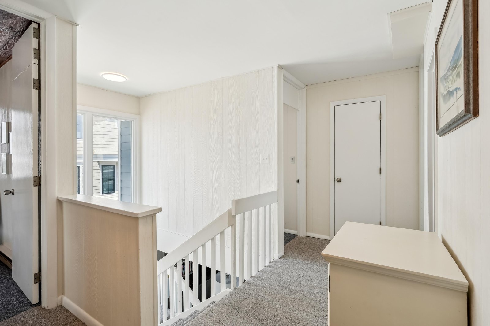 A bright second-floor landing connects the spaces in this charming property, featuring crisp white paneling, soft carpeting underfoot, and natural light streaming through the window.