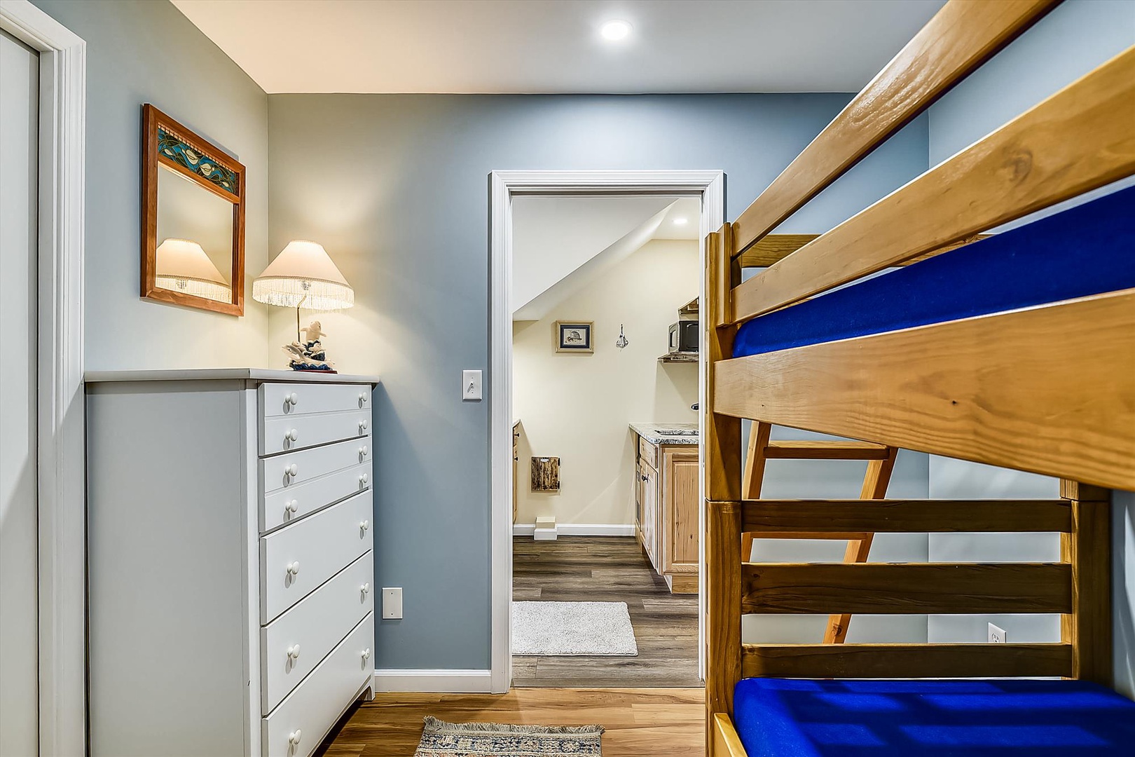 Your bright bedroom features a sturdy bunk bed with bold blue accents and ample storage in the white dresser, creating a cozy space for restful nights.
