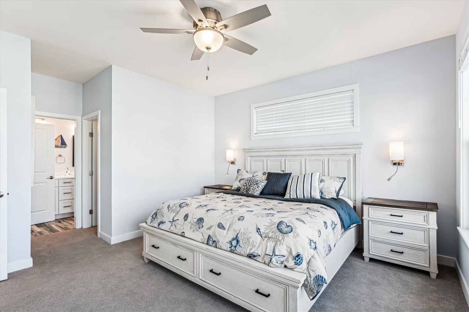 Drift off in this serene bedroom where soft coastal linens and soothing blue-gray tones create your perfect retreat. The ceiling fan keeps you comfortable while matching nightstands and an en-suite bath complete your private sanctuary.
